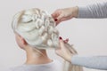 Beautiful girl with blonde hair, hairdresser weaves a braid close-up Royalty Free Stock Photo