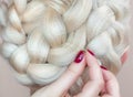 Beautiful girl with blonde hair, hairdresser weaves a braid close-up, in a beauty salon. Royalty Free Stock Photo