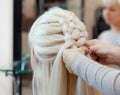 Beautiful girl with blonde hair, hairdresser weaves a braid close-up Royalty Free Stock Photo