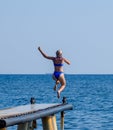 A beautiful girl in a blue bikini jumps from the pier into the water. Jumping in the sea Royalty Free Stock Photo