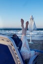 A beautiful girl in a blue bikini and a white hat is sunbathing on the beach, lying on a white chaise longue Royalty Free Stock Photo