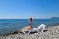 Beautiful girl in a blue bikini and white hat sunbathing on the beach, sitting on a white chaise lounge. Blonde with Royalty Free Stock Photo