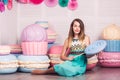 Beautiful girl in blue dress hold in hand huge candy in studio with decor of macaroons. Copy space.