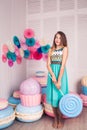 Beautiful girl in blue dress hold in hand huge candy in studio with decor of macaroons. Copy space.