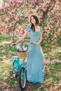 Beautiful girl in blue dress walk with bicycle in blooming spring garden Royalty Free Stock Photo