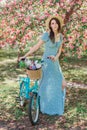 Beautiful girl in blue dress walk with bicycle in blooming spring garden