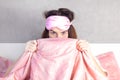 A beautiful girl with blue eyes sits in bed in pajamas and a sleep mask. Woman looks out from under the blanket Royalty Free Stock Photo