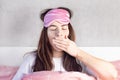 A beautiful girl with blue eyes sits in bed in pajamas and a sleep mask. Woman yawns in bed. She wants to sleep Royalty Free Stock Photo