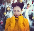 Beautiful girl with blue eyes in a yellow sweater under a snow-covered Christmas tree with Christmas toys. A girl in