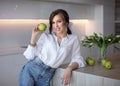 A beautiful girl in blue jeans and a white shirt holds a green Apple. Portrait of a young lady