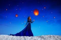 A beautiful girl in a blue long dress standing against the night sky with many Chinese sky lanterns flying wishes. Royalty Free Stock Photo