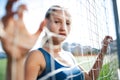 Beautiful girl in a blue shirt in leggings is on the football field is kept behind the net from the gate. Editorial sport concept. Royalty Free Stock Photo