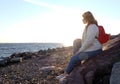 Beautiful girl body positive looking ahead on rocks seaside background in autumn season, red backpack, lifstyle