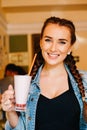 Beautiful girl with braids sitting in a cafe and drinking a milkshake, smiling at the camera Royalty Free Stock Photo