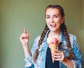 Beautiful girl with braids sitting in a cafe and eating huge multi-colored ice cream in a waffle cone. Smiling at the camera and