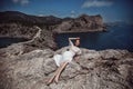 A beautiful girl, bride, in a white dress, barefoot lies on a rock against the background of a beautiful landscape, ocean and moun