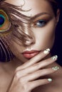 Beautiful girl with bright makeup, manicure design and peacock feather on her face. Art nails.