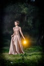 Beautiful girl with brown curly hair in wonderful dress with lamps light in fairytale forest. Art photo. Royalty Free Stock Photo