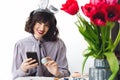 Beautiful girl in bunny ears talking on phone and smiling, painting easter egg at table with tulips in vase. Stylish young Royalty Free Stock Photo