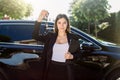 Beautiful girl with car key in hand. Caucasian woman car seller holding car keys, standing in front of new black car Royalty Free Stock Photo