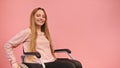 Beautiful girl in casual clothing smiling in the wheelchair. Isolated on pink background Royalty Free Stock Photo