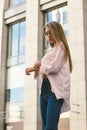 Beautiful girl in city near modern building. Soft daylight. Attractive girl with long hair looking at the watch. Royalty Free Stock Photo