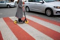 Beautiful Girl In A Coat Rides Electric Scooter on a pedestrian crossing In The City Royalty Free Stock Photo