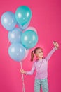 A beautiful girl with colorful balloons is laughing at the pink background. A girl takes photos of herself on her phone. A joyous