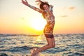 Beautiful girl in colorful dress jumping in ocean water in sunset