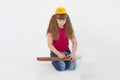 A beautiful girl in a construction cap, a hard hat with a screwdriver, a drill in her hands repairs a wooden stick on a white back