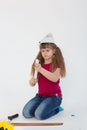 A beautiful girl in a construction cap, a hard hat with a screwdriver, a drill in her hands repairs a wooden stick on a white back