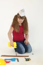 A beautiful girl in a construction cap, a hard hat with a screwdriver, a drill in her hands repairs a wooden stick on a white back