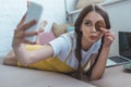 beautiful girl with cookie taking selfie on smartphone while lying on sofa Royalty Free Stock Photo