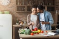 Beautiful girl cooking while her boyfriend kissing her in cheek Royalty Free Stock Photo