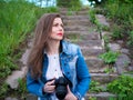 Beautiful girl in a cotton jacket sits on vintage stone steps and taking photos with a professional camera in windy weather