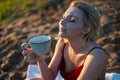 A beautiful girl, covered with a plaid in the evening at sunset, holds a mug of tea with two hands against the sea Royalty Free Stock Photo