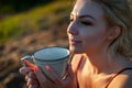 A beautiful girl, covered with a plaid in the evening at sunset, holds a mug of tea with two hands against the sea Royalty Free Stock Photo