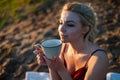 A beautiful girl, covered with a plaid in the evening at sunset, holds a mug of tea with two hands against the sea Royalty Free Stock Photo