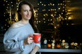 Beautiful girl in a cozy sweater enjoying a cup of coffee in anticipation of christmas, happy carefree life.