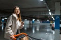 Beautiful girl with cup of coffee and trolley in the underground parking of shopping mall.