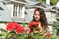 Beautiful girl with curls next to red roses in the garden