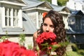 Beautiful girl with curls next to red roses in the garden