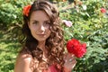 Beautiful girl with curls next to red roses in the garden