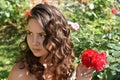 Beautiful girl with curls next to red roses in the garden