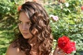 Beautiful girl with curls next to red roses in the garden