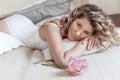 Beautiful girl with curly hair in a white bodysuit with a rose lies on the bed Royalty Free Stock Photo