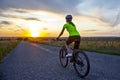 Beautiful girl cyclist rides a bicycle on the road in the sunset Royalty Free Stock Photo