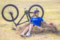 Beautiful girl cyclist sitting on dry grass on the background of the bike. Nature and man Royalty Free Stock Photo