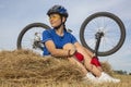 Beautiful girl cyclist sitting on dry grass on the background of the bike. Nature and man Royalty Free Stock Photo