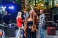 Beautiful girl dancing at foreground while her friends dancing in light of colored lamps during celebration party